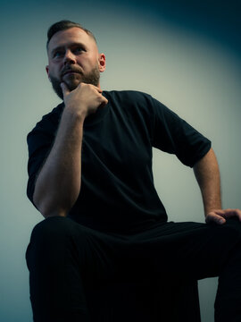 Man in Black Shirt Posing With Hand on Chin in Studio Setting