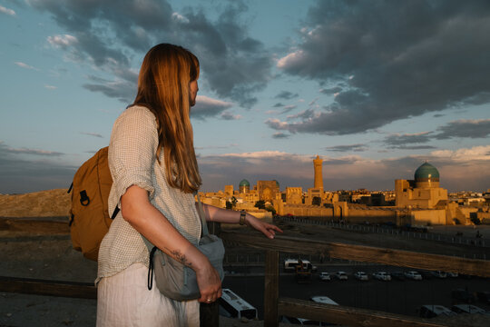 Woman overlooking the historic skyline of Bukhara at sunset.