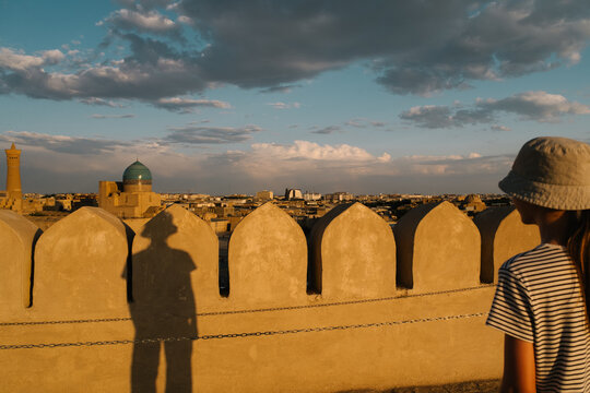 Girl looking over a wall at the historic Bukhara skyline at sunset.