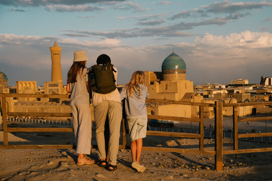 A father and two daughters overlook the Bukhara skyline at sunset.