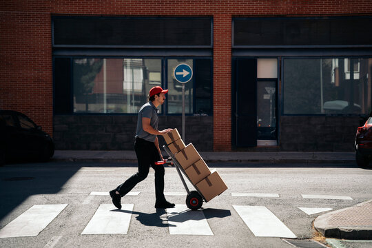Courier delivering packages on hand truck across street