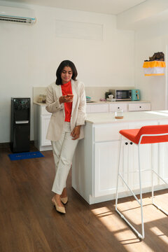 Businesswoman using smartphone in office kitchen