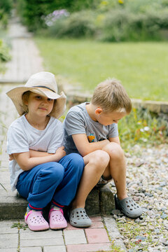 Children are sitting together outside on the garden path.