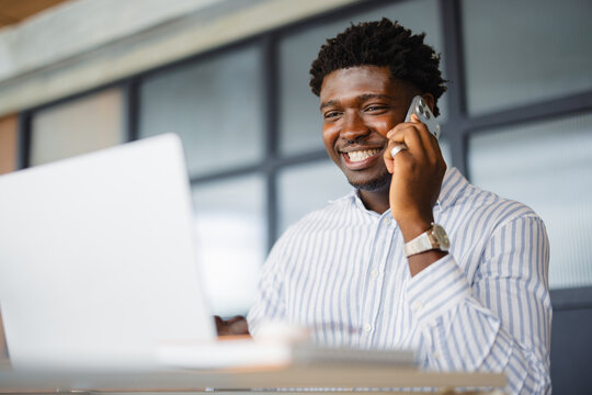Man Speaks on Phone While Working on Laptop in Modern Office Space