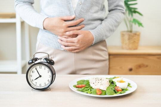 Intermittent fasting, diet healthy asian young woman dietary, having stomach ache, temptation hungry of brunch food in morning on table at home, waiting time to eat salad but not yet time first meal.