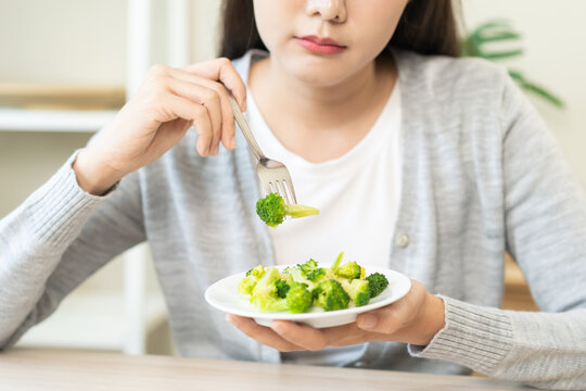 Diet in bored concept, Ketogenic, Low carb, Intermittent Fasting young woman dieting holding fork at broccoli on salad plate tired with eat fresh vegetables. Nutrition clean, healthy food good taste.