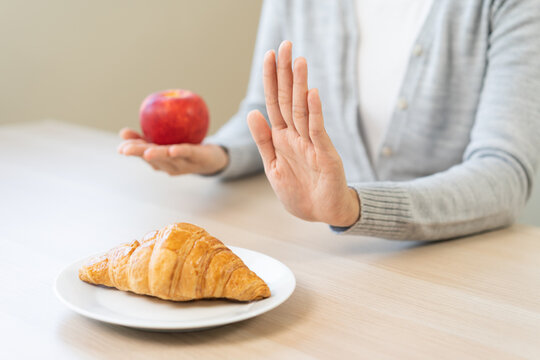 Ketogenic, Low carb, Intermittent Fasting Diet hand push out, refuse butter croissant bread on plate choose apple for good food, fighting to keep it from getting fat. Healthy nutrition of weight loss.