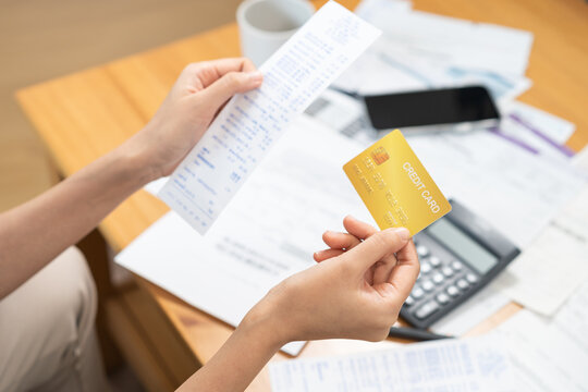 Financial owe, stressed asian woman, girl hand holding credit card, stressed by calculate expense from invoice or bill, no money to pay, mortgage or loan on table at home. Debt, bankruptcy or bankrupt
