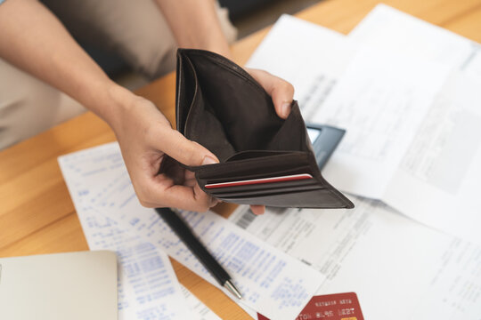 Close up of a person holding an empty leather wallet over bill invoice and credit card on wooden table, concept of financial crisis, bankruptcy, debt problem and economic depression at home.