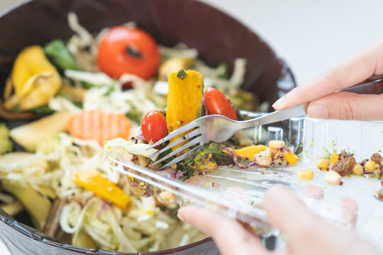Compost from leftover food asian young housekeeper woman, female hand holding salad box use fork scraping waste, rotten vegetable throwing away into garbage, trash or bin. Environmentally responsible