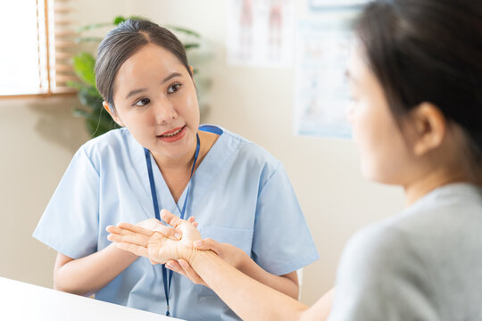 Asian young woman physical therapist examining and massaging a patient trigger fingers and wrist for hand joint rehabilitation, arthritis diagnosis and office syndrome occupational therapy concept.