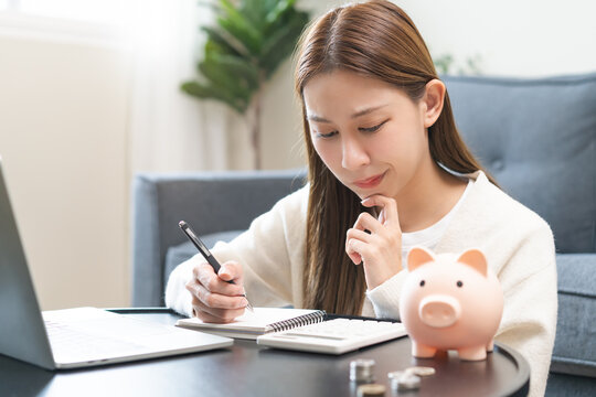 Financial, asian young woman, girl putting stack coins on table for calculate cost sitting in living room at home, financial plans to spend enough money on his income for saving money and payment.
