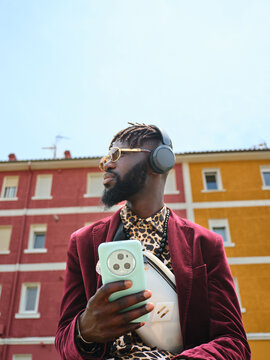Stylish Black man listening music on headphones in urban setting