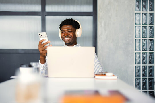 Man Sits at Desk Using Phone While Smiling During Work Hours