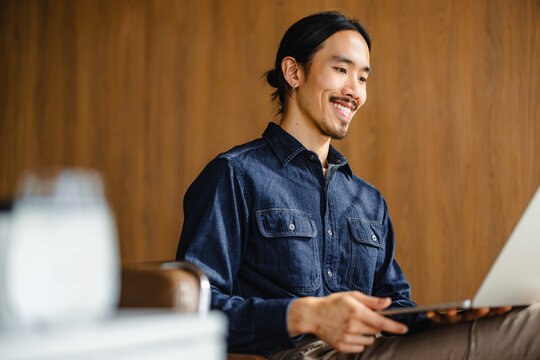 Man Smiles While Using Laptop in Cozy Indoor Space