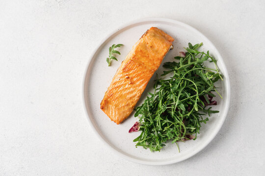 Fresh baked salmon fillet glazed with honey mustard sauce served with green arugula salad on a white plate with copy space. High protein healthy meal