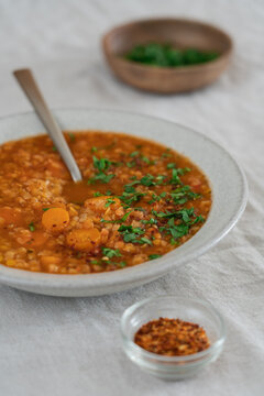 Hearty lentil soup served in a rustic bowl on a natural linen tablecloth. High protein comfort food concept featuring fiber-rich legumes, wholesome ingredients and nourishing homemade meal
