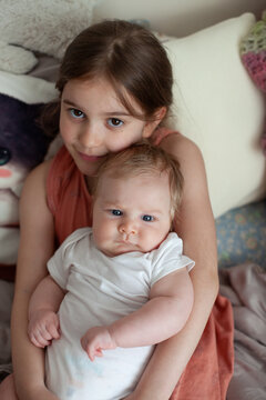 A young girl holds her newborn sibling on a soft bed at home