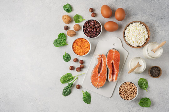 High protein food set with fresh salmon, eggs, cottage cheese, yogurt, lentils, chickpeas, beans and nuts arranged on white background with copy space. Healthy wellness nutrition concept 