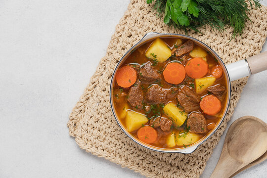Homemade stew in enamel pot on light background, top view seasonal comfort food concept