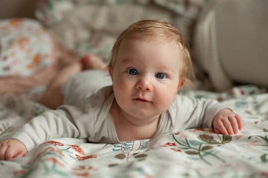 A baby does tummy time on a floral patterned bedsheet