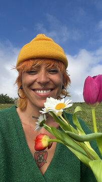 Smiling person holding flowers in a green field under blue sky