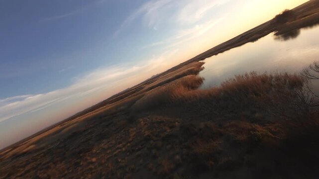 Dramatic drone shot over a lake surrounded by long grasses at sunset