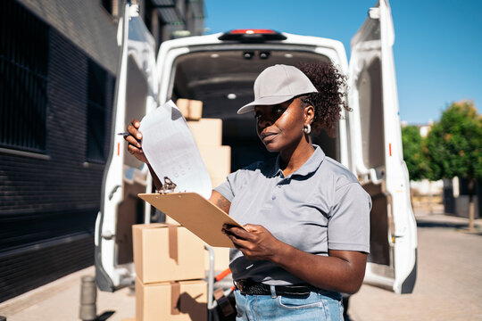 Female courier checking delivery packages standing by van