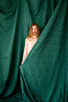 Woman with closed eyes behind damask curtain