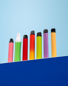 Colorful disposable electronic cigarettes and vape pens lined up against a bright blue background.