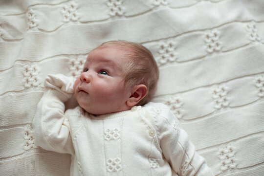 A newborn gazes upward dressed in cream knitwear