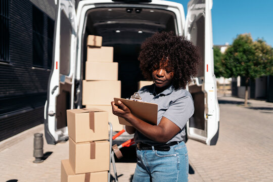 Female courier checking delivery packages standing by van