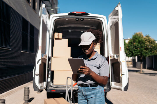 Black delivery woman checking packages on tablet