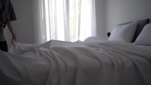 Slow motion video of a woman making a bed with a soft blanket, cozy bedroom and peaceful home routine
