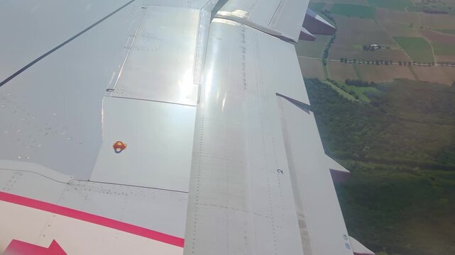 Aircraft wing with visible winglet and orange light indicator during descent over green landscape and highway, showcasing the transition in altitude and perspective