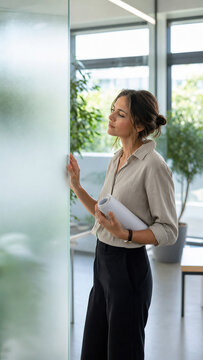 Woman architect inspecting sandblasted glass partition in modern office. Professional interior designer examining frosted decor element. Construction material and renovation concept.