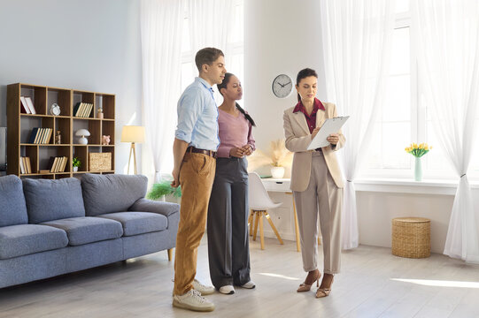 Agent couple presentation during viewing and agreement. In a bright apartment agent explains rental terms, showing a clipboard as the couple in discussion. Clear concept of property decision.