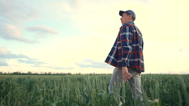 The man walks through the green field, observing the landscape. The man looks towards the horizon, contemplating the vast expanse of the field.