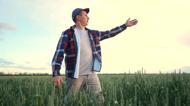 The man walks through a green field, observing his surroundings as he moves. The man appears thoughtful while enjoying the serene landscape.