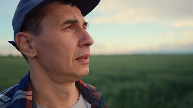The man stands in the field, gazing thoughtfully at the horizon. The man in a cap appears contemplative amidst the expansive green landscape.