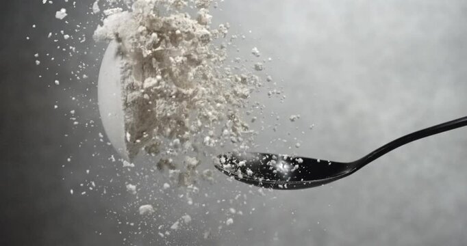 Dry milk powder falling from black spoon in super slow motion