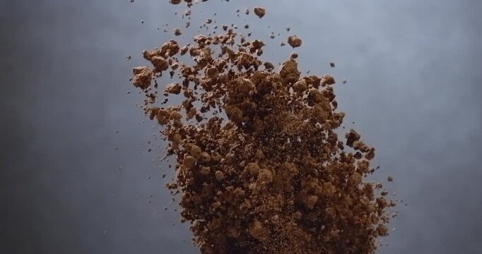 Cocoa powder bursts from wooden spoon creating flying chocolate dust cloud slow motion