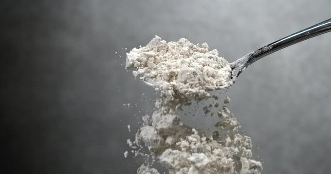 Flour falling from black spoon in super slow motion