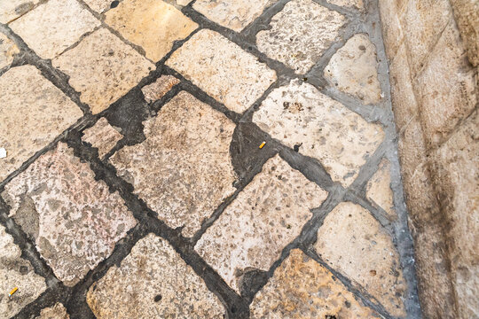 Close up of old cobblestone pavement with weathered stone blocks and dark grout lines