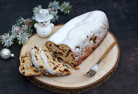 Traditional German Christmas stollen, sliced, on a wooden board with Christmas decorations.