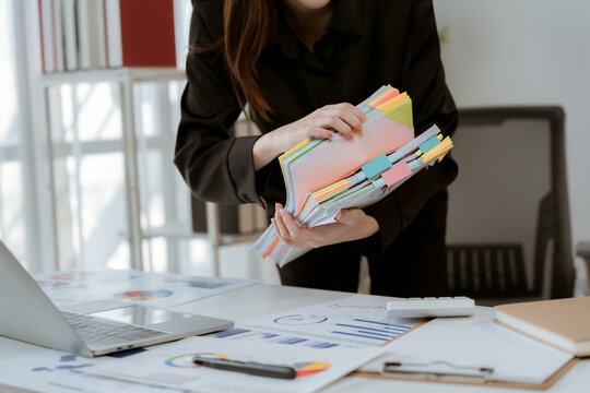 Organized Files in Office: A focused professional sorts through a stack of colorful documents and folders, meticulously organizing information on a modern office desk.