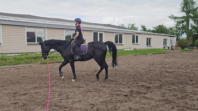 Training a horse in an outdoor riding arena with a rider using a lunge line on a cloudy day
