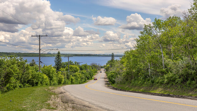 Scenic Road Descending Towards Manitou Lake and Core Manitou Beach Town in Saskatchewan, Canada Under a Dramatic Summer Cloud-Filled Sky.