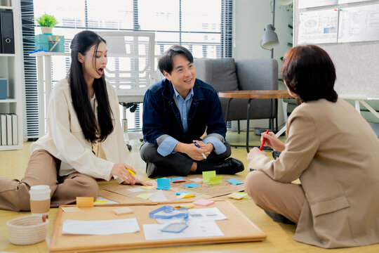 Business team brainstorming with sticky notes on floor, casual creative discussion during startup workshop, colleagues sharing ideas and collaborating on project board concept