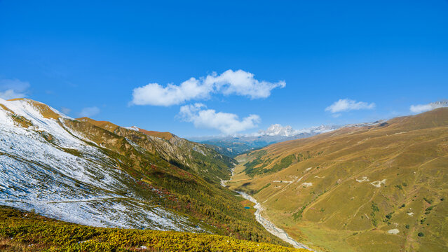 Landscape photograph of wide Adishi valley with river under bright blue sky viewed from Chkhutnieri pass in Svaneti Georgia.
